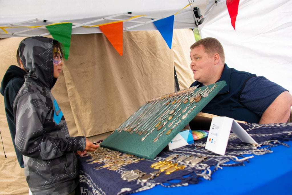 From left: Blake Bailey peruses coin jewelry and accessories made by Russell Minor. On Friday, July 12, 2019, Minor brought his handicrafts to the Copper River Salmon Jam festival for the first time. Photo by Zachary Snowdon Smith/The Cordova Times