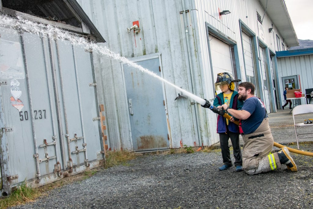Lt. Stephen Phillips assists Tracer Stimson, 8, in a fire hose exercise. (Oct. 19, 2019) Photo by Zachary Snowdon Smith/The Cordova Times